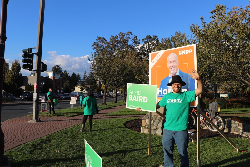Nick holding a Gord Baird BC Green election size, with a Horgan sign in the background.